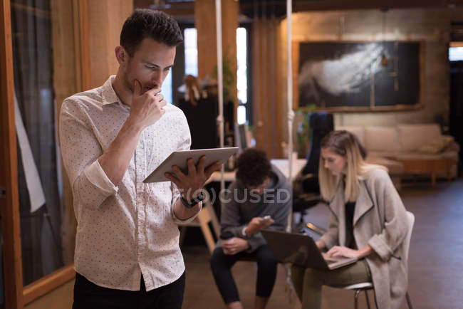 Männliche Führungskraft nutzt digitales Tablet mit Kollegen im Hintergrund im Bürobereich. — Stockfoto