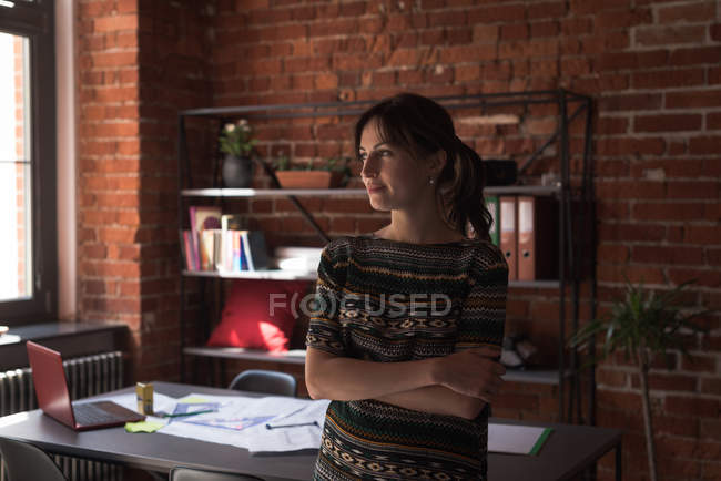 Young female executive standing arms crossed in office — Stock Photo
