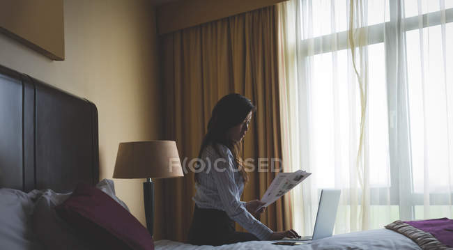Businesswoman reading documents while working on laptop in hotel room — Stock Photo