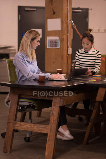 Dirigenti femminili che utilizzano laptop e tablet digitale alla scrivania in ufficio
. — Foto stock