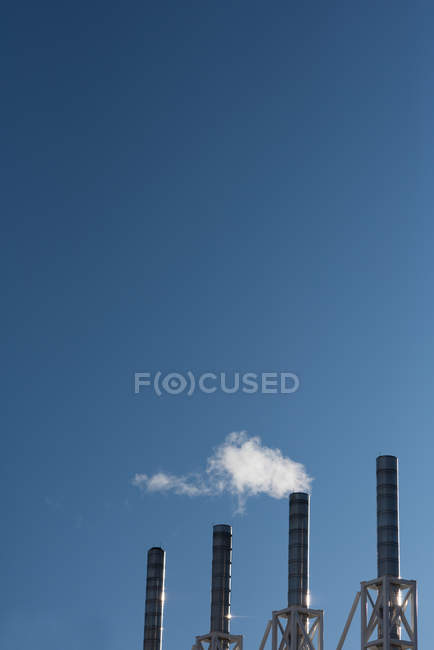 Humo saliendo de la chimenea de la fábrica contra el cielo despejado - foto de stock