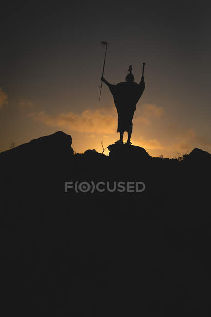 Silueta del hombre maasai de pie sobre la roca durante el atardecer - foto de stock