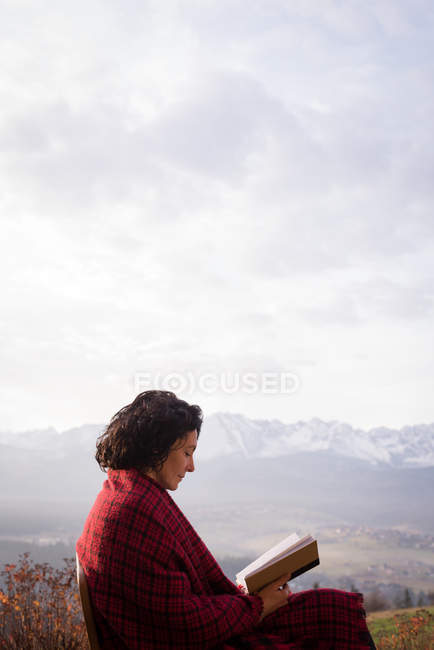 Жінка загорнута в ковдру читає книгу в туманний день — стокове фото