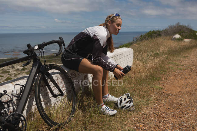 Motociclista donna con bottiglia d'acqua seduta su una panchina di roccia in una giornata di sole — Foto stock