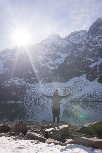 Female hiker standing with arms crossed at lakeside during winter — Stock Photo
