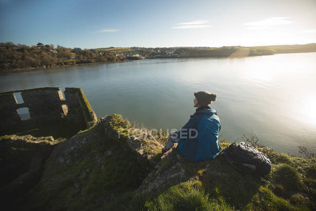 Vue arrière du randonneur masculin se relaxant près du lac à la campagne — Photo de stock