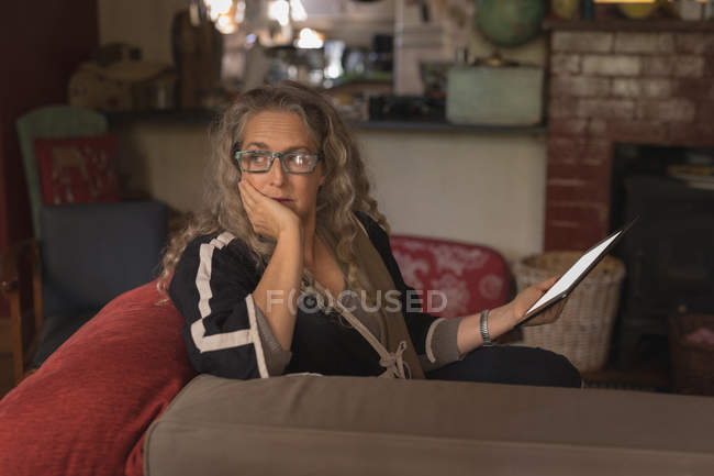 Продумана зріла жінка сидить з цифровим планшетом на дивані — стокове фото