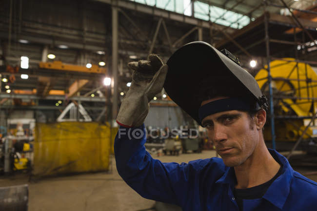 Retrato de soldador seguro que sostiene el casco de soldadura en el taller - foto de stock