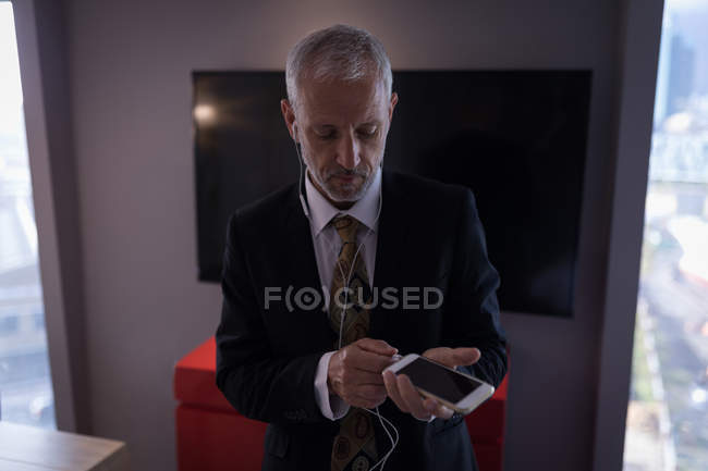 Uomo d'affari che collega gli auricolari allo smartphone in una stanza d'albergo — Foto stock