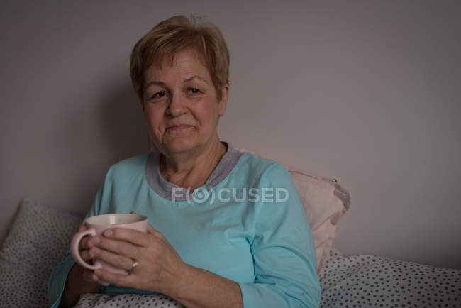 Старшая женщина пьет кофе в спальне дома — стоковое фото