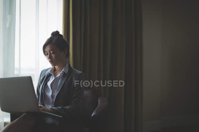 Mujer de negocios usando el ordenador portátil mientras está sentado en el sillón en la habitación de hotel - foto de stock