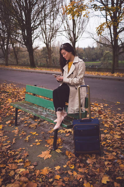 Donna d'affari utilizzando il telefono cellulare mentre seduto sulla panchina durante l'autunno — Foto stock