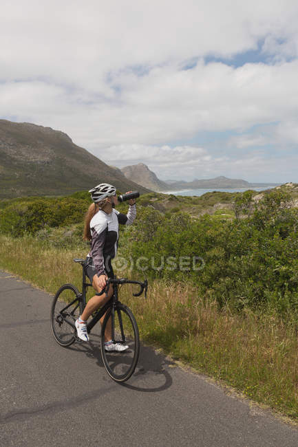 Biker donna acqua potabile da bottiglia su strada in una giornata di sole — Foto stock