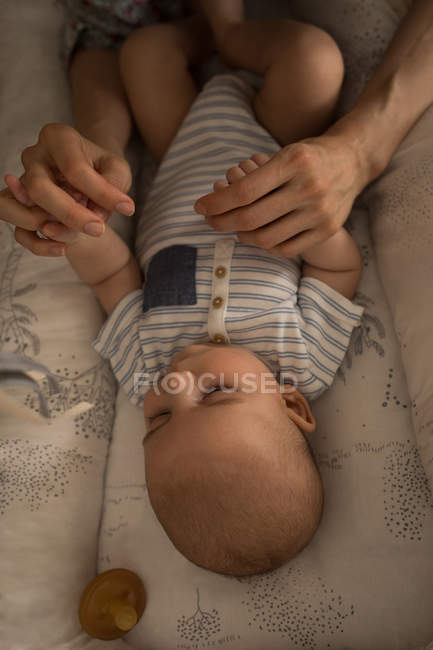 Nahaufnahme des niedlichen kleinen Babys, das auf dem Bett liegt und die Hände der Mutter zu Hause hält — Stockfoto