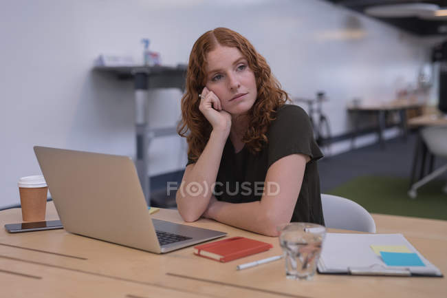 Задумчивая женщина-руководитель сидит за столом в офисе — стоковое фото