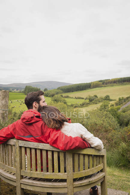 Pareja sentada en el banco en el campo - foto de stock