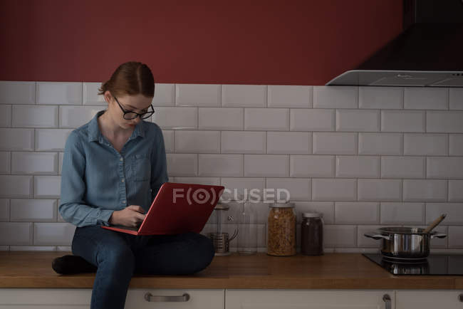 Jeune femme utilisant un ordinateur portable dans la cuisine — Photo de stock