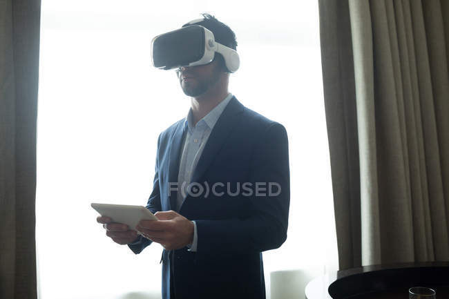 Hombre de negocios que usa auriculares de realidad virtual con tableta digital en la habitación de hotel - foto de stock