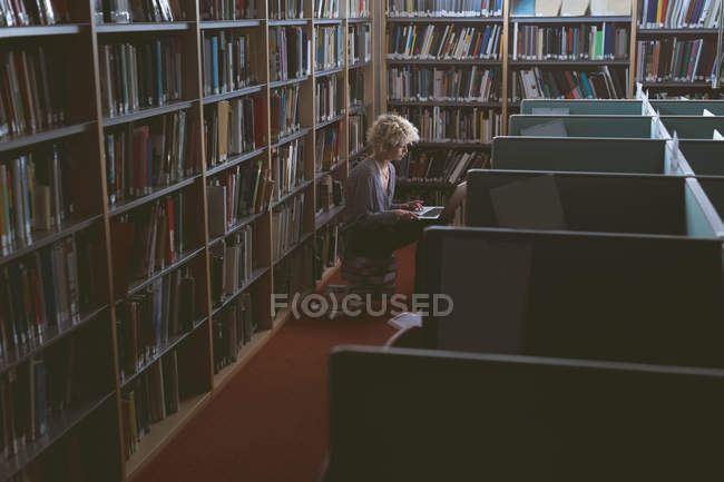 Jeune femme utilisant un ordinateur portable dans la bibliothèque — Photo de stock