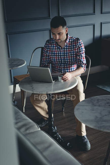 Бизнесмен пьет кофе во время использования ноутбука в офисе — стоковое фото