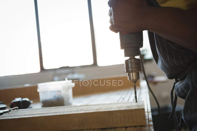 Charpentier forant la planche en bois avec la machine en atelier — Photo de stock