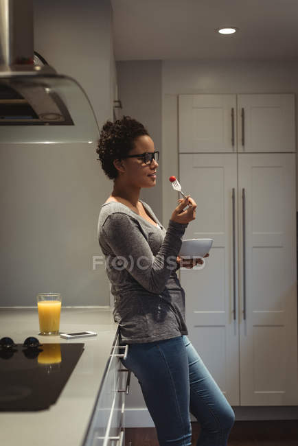 Молода вагітна жінка спирається на кухонний лічильник, маючи їжу — стокове фото
