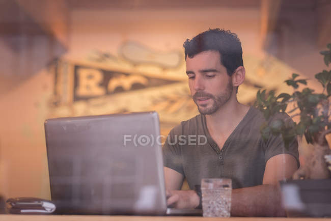 Metà uomo adulto utilizzando il computer portatile in caffè dietro la finestra . — Foto stock
