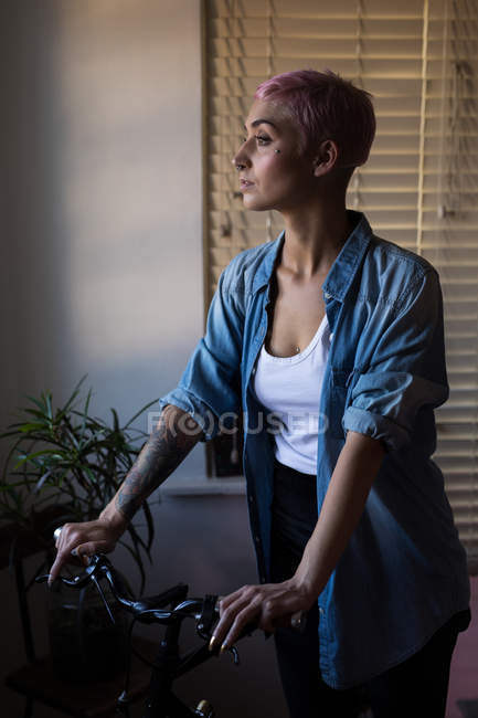 Stylish woman standing with bicycle at home. — Stock Photo