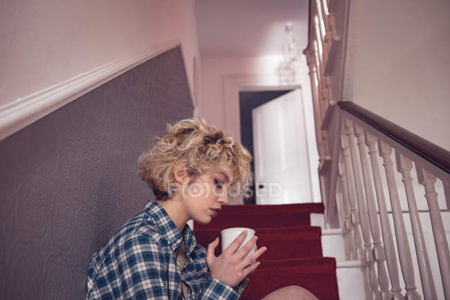 Junge Frau rasiert Kaffee im Treppenhaus zu Hause — Stockfoto