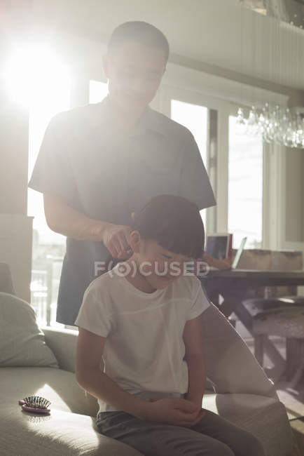 Padre peinando el pelo de sus hijas en la sala de estar en casa - foto de stock
