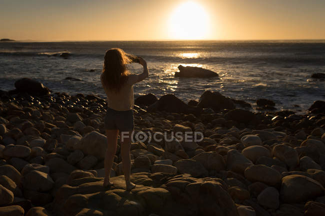 Mulher tirando foto do mar com telefone celular durante o pôr do sol — Fotografia de Stock
