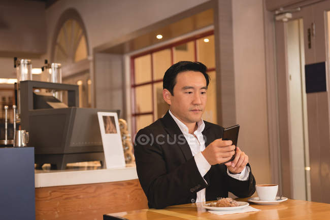 Homme d'affaires utilisant un smartphone tout en prenant un café dans un café — Photo de stock