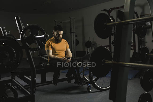 Homme handicapé vérifiant smartphone sur banc de presse dans la salle de gym — Photo de stock