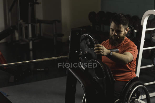 Hombre discapacitado ajustando la barra en el gimnasio - foto de stock