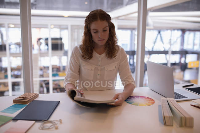 Female graphic designer reading a book in office — Stock Photo