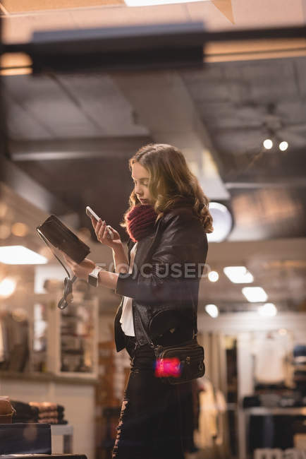 Девушка с помощью мобильного телефона при выборе сумки в торговом центре — стоковое фото
