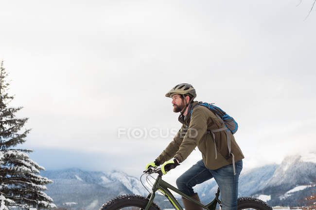 Homem andando de bicicleta na paisagem montanhosa nevada durante o inverno . — Fotografia de Stock