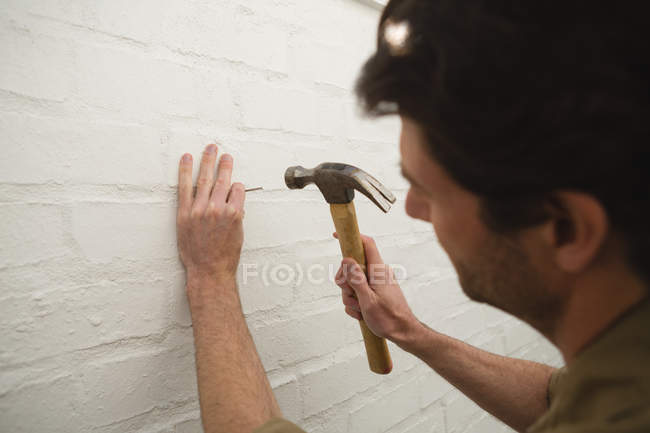 Close-up de carpinteiro masculino martelando unha na parede — Fotografia de Stock