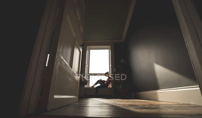 Woman reading book on window sill at home — Stock Photo