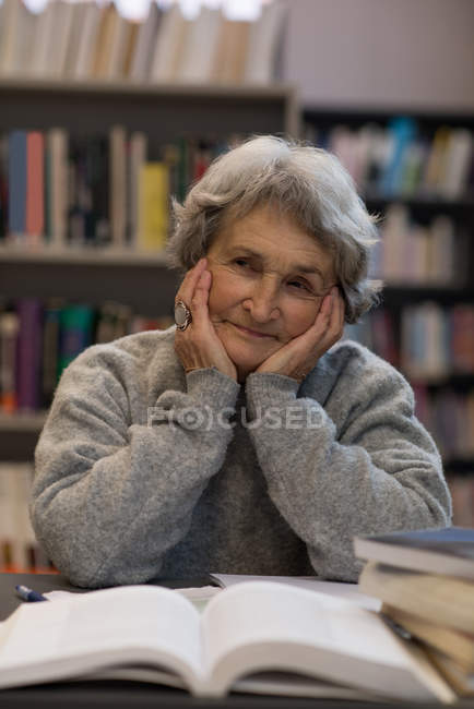 Задумчивая пожилая женщина улыбается в библиотеке — стоковое фото