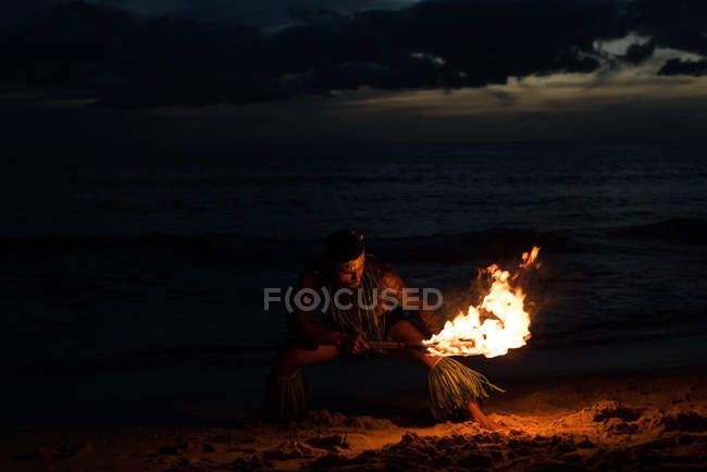 Male fire dancer performing with burning fire levi stick on beach at night — Stock Photo