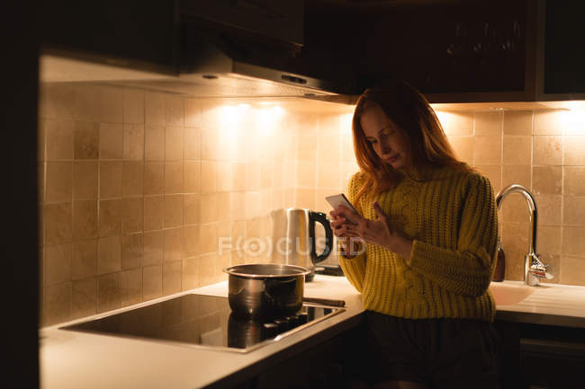 Mulher usando telefone celular na cozinha em casa — Fotografia de Stock