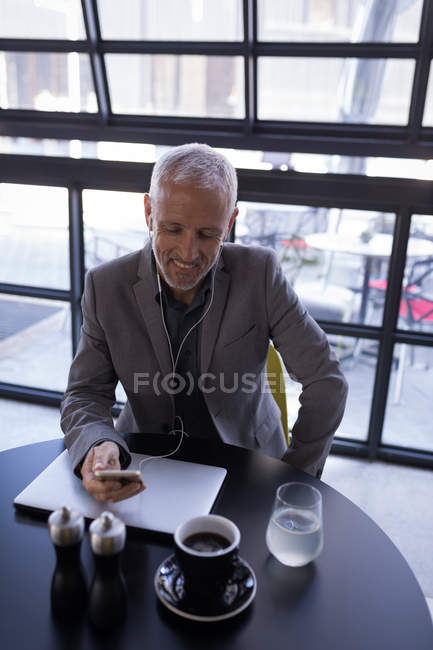 Geschäftsmann benutzt Mobiltelefon während er in der Hotellobby am Laptop arbeitet — Stockfoto