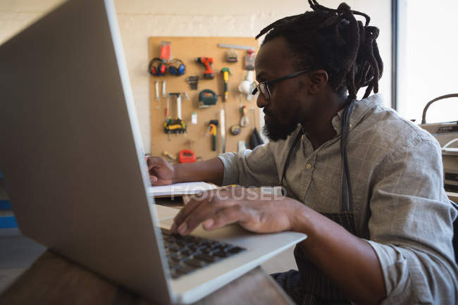Carpinteiro usando laptop à mesa na oficina — Fotografia de Stock