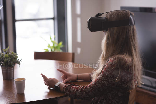 Жіночий керівник використовує гарнітуру віртуальної реальності зі скляним цифровим планшетом в офісі — стокове фото