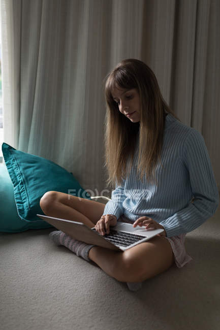 Junge Frau mit überkreuzten Beinen mit Laptop zu Hause. — Stockfoto