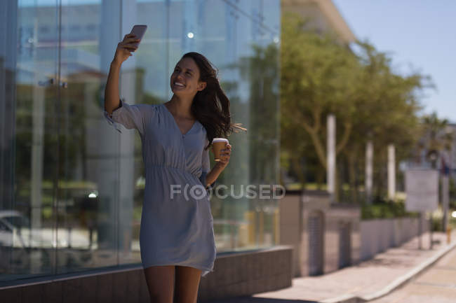 Young woman taking selfie with mobile phone outdoors — Stock Photo