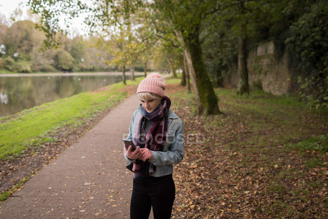 Junge Frau in warmer Kleidung benutzt ihr Handy im Park — Stockfoto