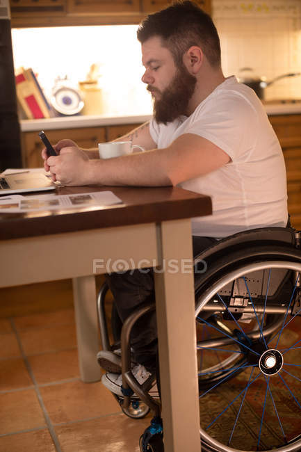 Homme handicapé utilisant un téléphone portable tout en travaillant sur un ordinateur portable à la maison — Photo de stock