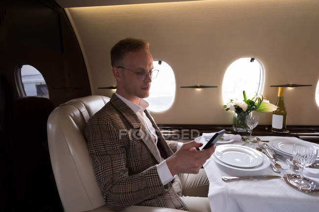 Hombre de negocios atento utilizando el teléfono móvil en jet privado - foto de stock